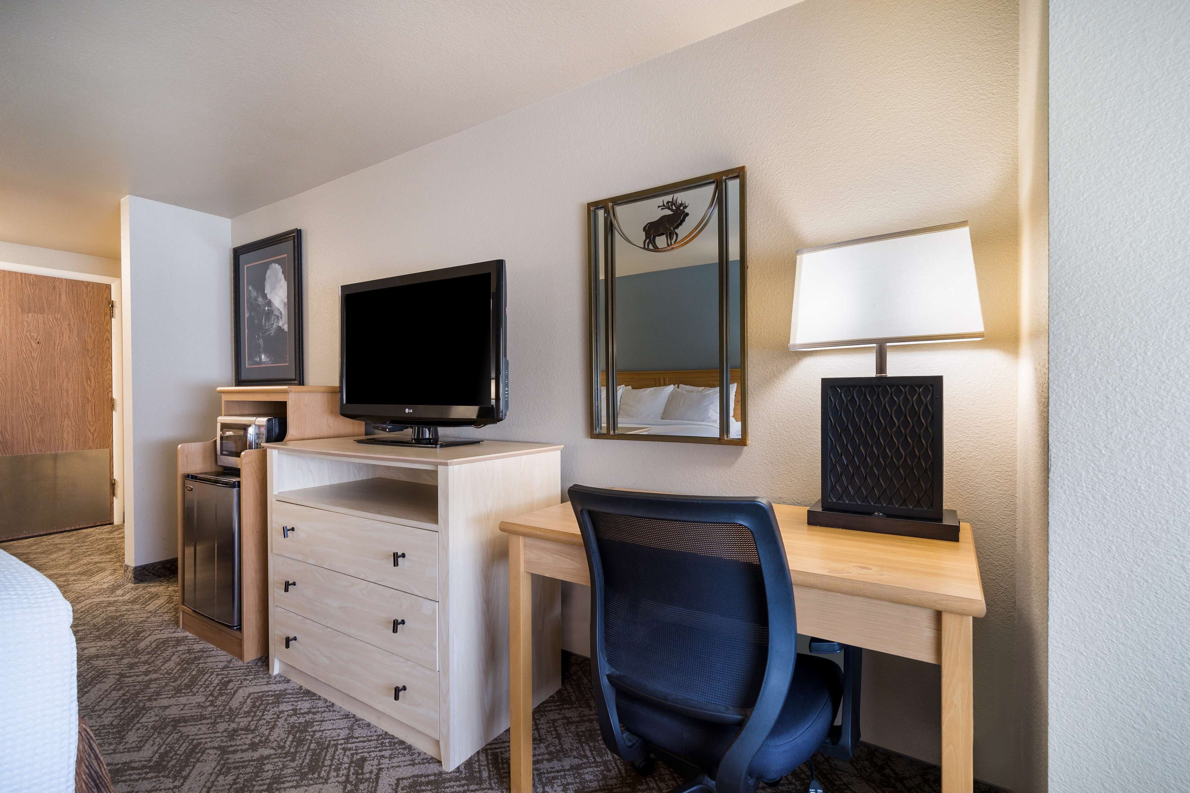 A hotel room with a bed, a desk with a computer, a television, a mirror, and a lamp.