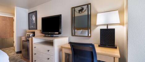 Una camera d'albergo con un letto, una scrivania con un computer, una televisione, uno specchio e una lampada.