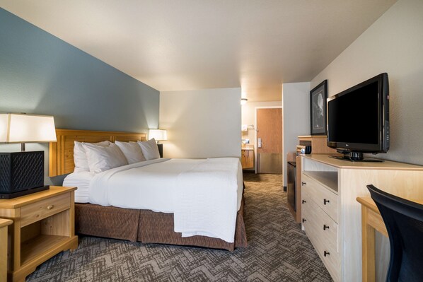 A hotel room with a bed, a desk with a TV, a lamp, and a dresser.