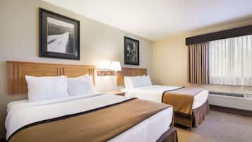 Een hotelkamer met twee bedden, een houten hoofdbord, een ingelijste foto aan de muur, een lamp en een raam met gordijnen.