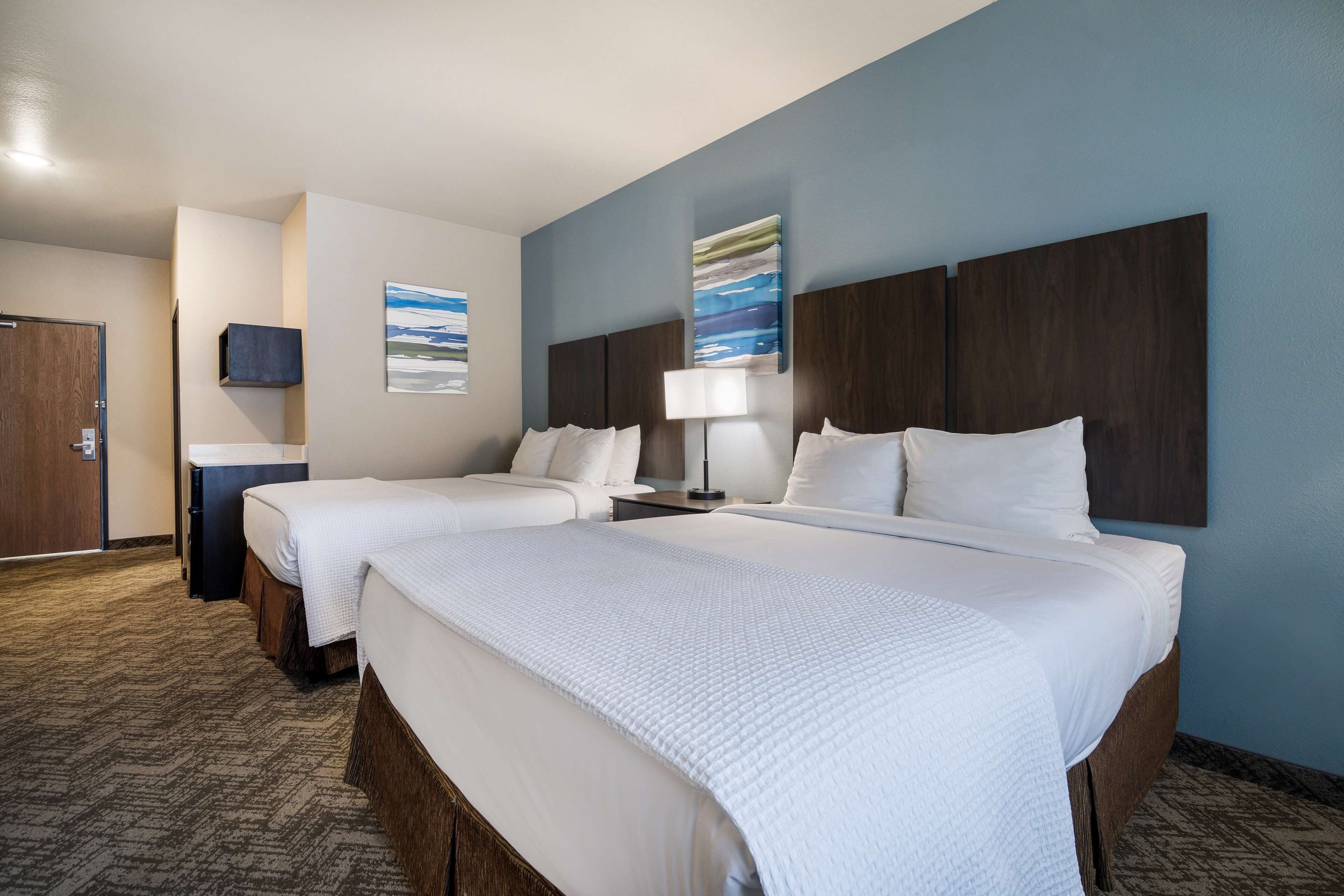 Quarto de hotel com duas camas, uma escrivaninha, uma cadeira, televisão e obras de arte nas paredes.