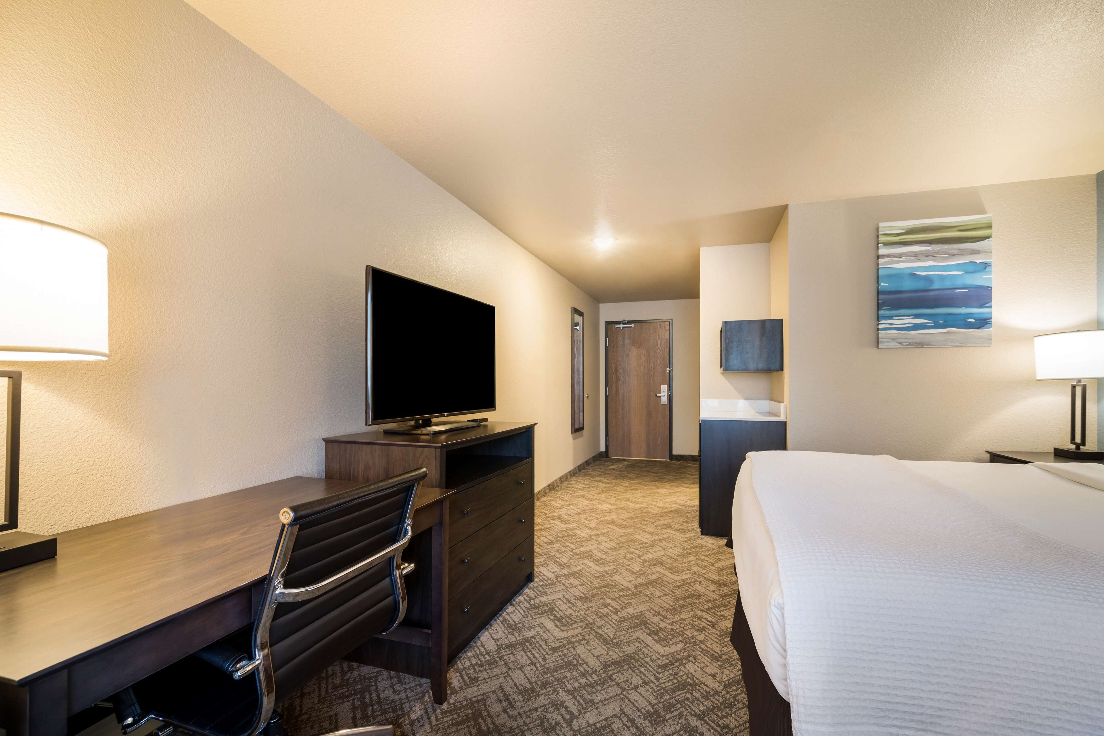 A hotel room with a bed, a desk with a chair, a television, and a painting on the wall.