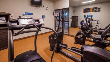 Gimnasio de hotel con cintas de correr, elípticas y un espejo grande.