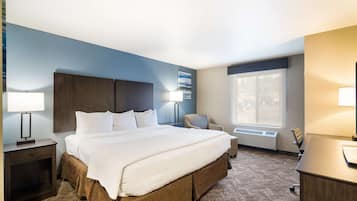 A hotel room with a large bed, a desk, a chair, a window, and a wall-mounted air conditioner.