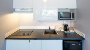 A modern kitchen with a black countertop, stainless steel sink, built-in microwave, and a dishwasher. - Cassandra Hotel (Vancouver)