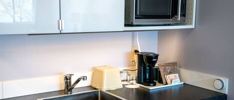 A kitchen with a built-in microwave, a coffee maker, a toaster, and a sink.