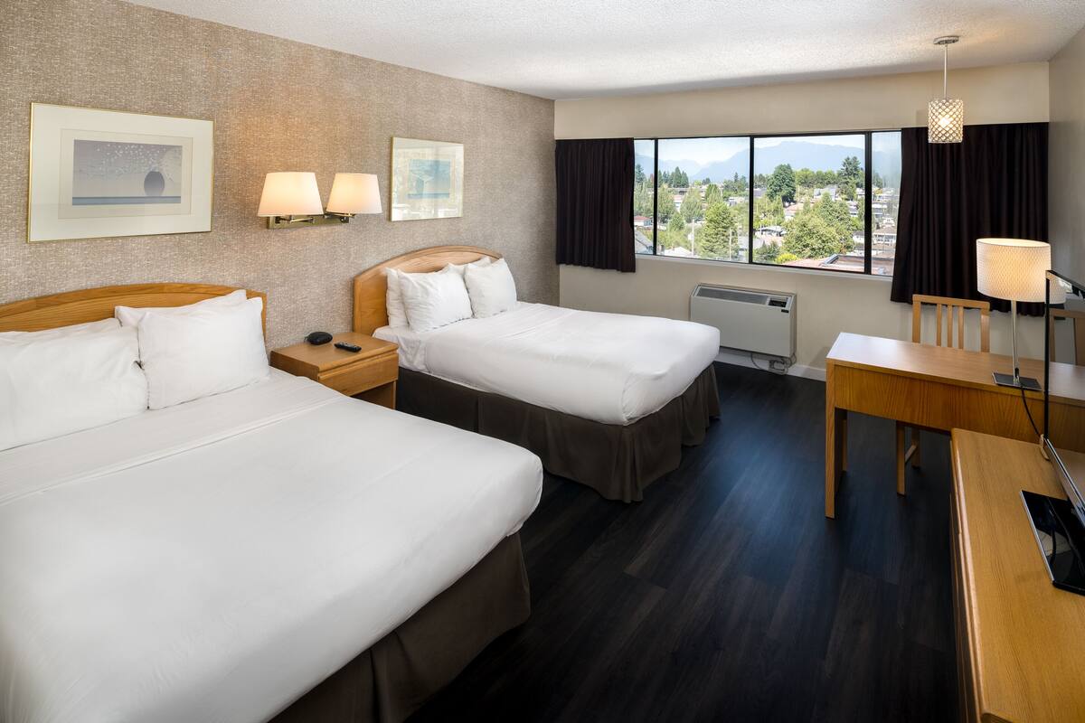Habitación de hotel con dos camas, un escritorio, una silla, una ventana con vistas y dos lámparas de pared.