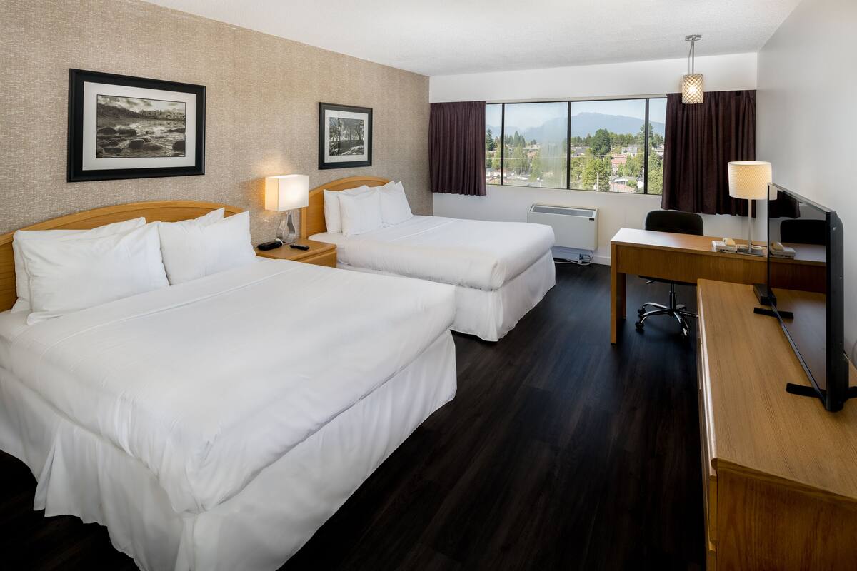 Habitación de hotel con dos camas, un escritorio, una silla, una lámpara, un marco de fotos y ventana con vistas.