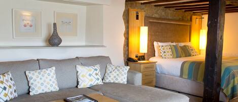 A cozy room with a sofa, a wooden coffee table, a bed with a striped blanket, and a stone wall.