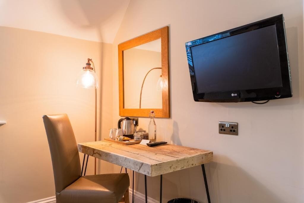 A small room with a wooden table, a chair, a television mounted on the wall, and a lamp.