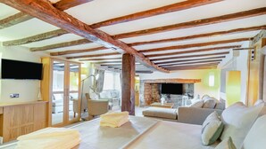 Una sala de estar acogedora con chimenea de piedra, televisor de pantalla plana montado en la pared y un área de estar confortable con sofá y sillones.