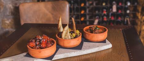 Three terracotta bowls with food on a wooden table, set against a backdrop of wine bottles.