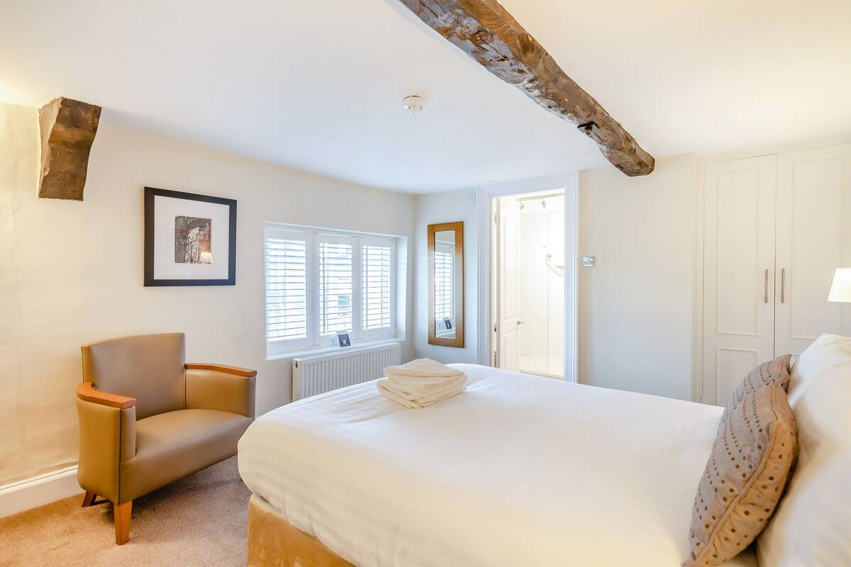 A bedroom with a bed, a chair, a radiator, and a window with blinds.