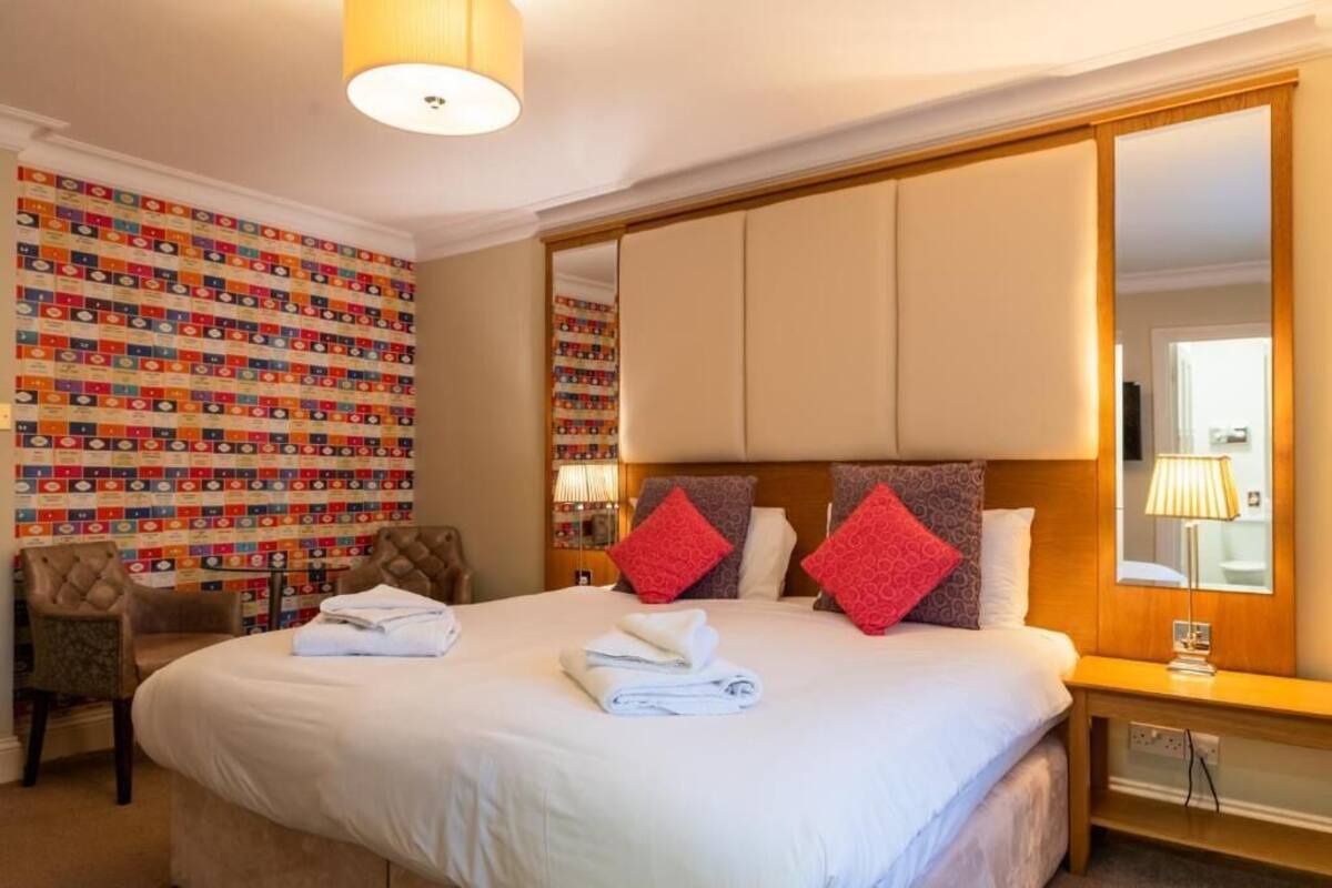 A hotel room with a large bed, a mirror, a wall with colorful patterns, and a wooden nightstand.