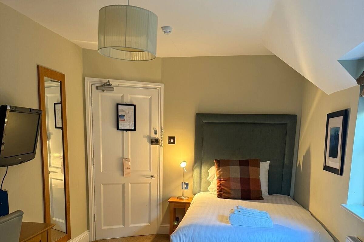 A bedroom with a bed, a dresser, a television, a door, and a ceiling light.