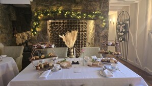 Mesa lista para una comida con un muro de piedra de fondo, luces decorativas y un arreglo floral.