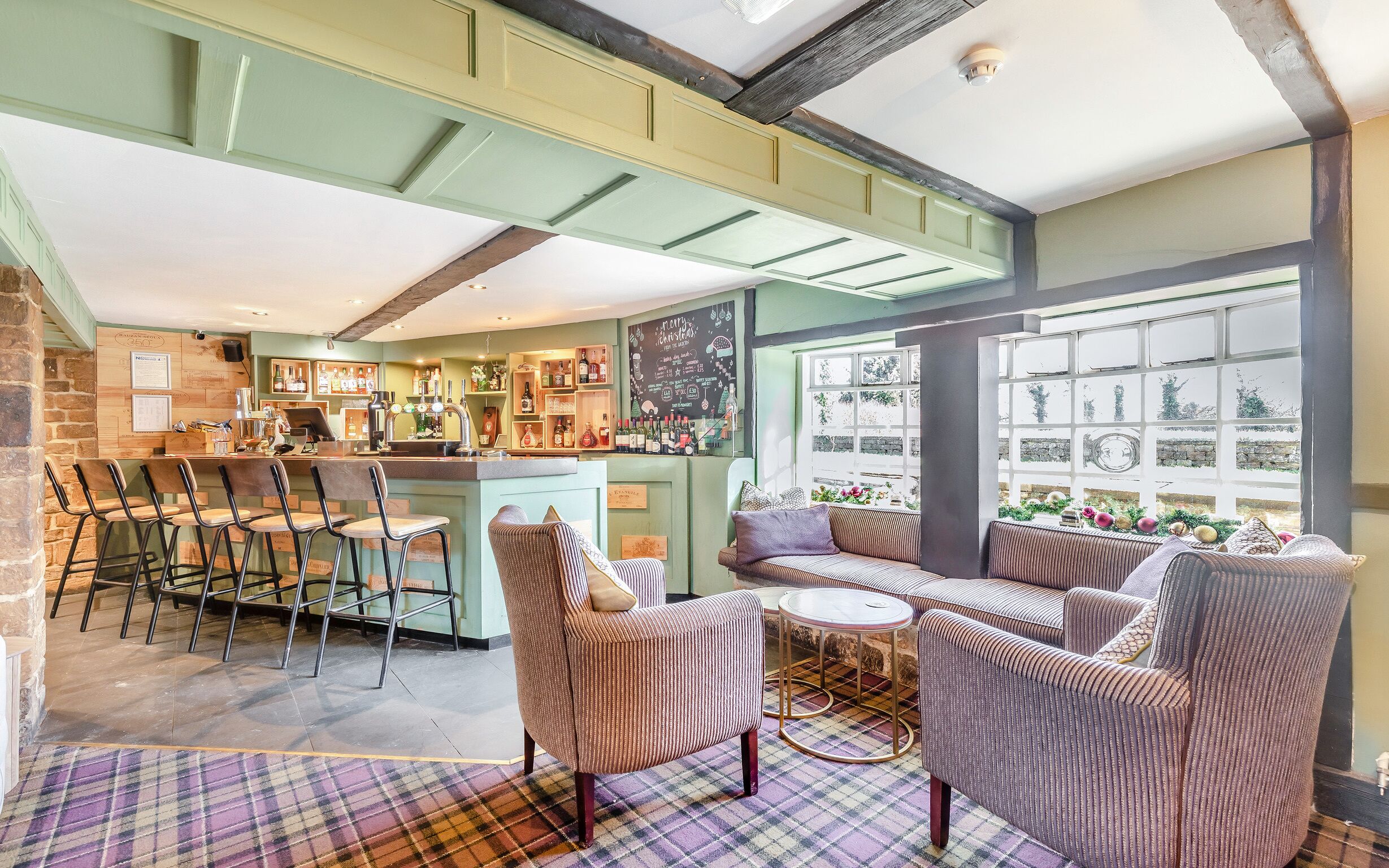 A bar area with stools, a counter, and a chalkboard menu. There are cushioned seating areas with a plaid carpet.