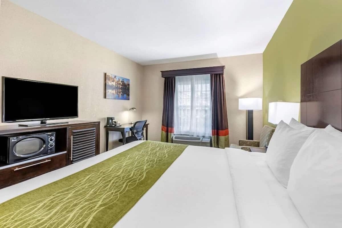 Habitación de hotel con cama, televisor, escritorio y ventana con cortinas.