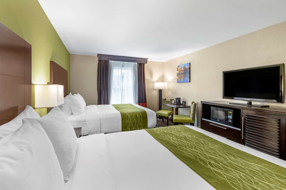Habitación de hotel con dos camas, televisión, escritorio con ordenador y ventana con cortinas.