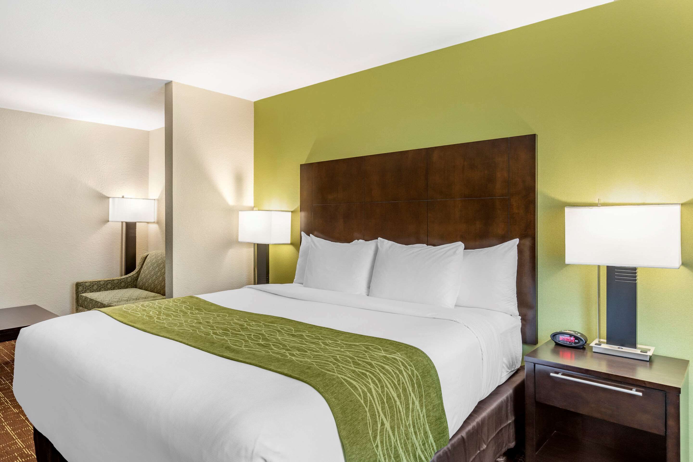 Een hotelkamer met een groot bed, twee nachtkastjes met lampen, een stoel en een groene wand.