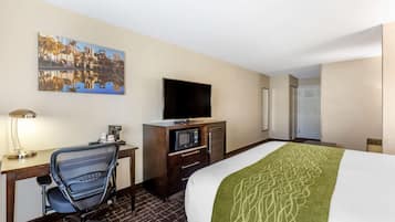 Une chambre d’hôtel avec un lit, un bureau et une chaise, une télévision, un four à micro-ondes et un tableau au mur.