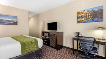 A hotel room with a bed, a desk with a chair, a television, and artwork on the walls.