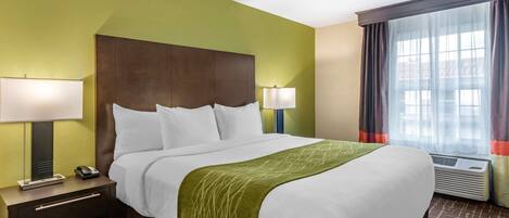 Habitación de hotel con una cama grande, dos mesitas de noche, una lámpara, un equipo de aire acondicionado y una ventana con cortinas.