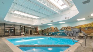 An indoor swimming pool with a mural of a desert landscape, a ceiling with skylights, and a seating area with chairs. - Grand Vista Hotel (Grand Junction)
