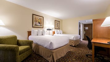 A hotel room with two beds, a desk, a chair, a lamp, and a picture on the wall.