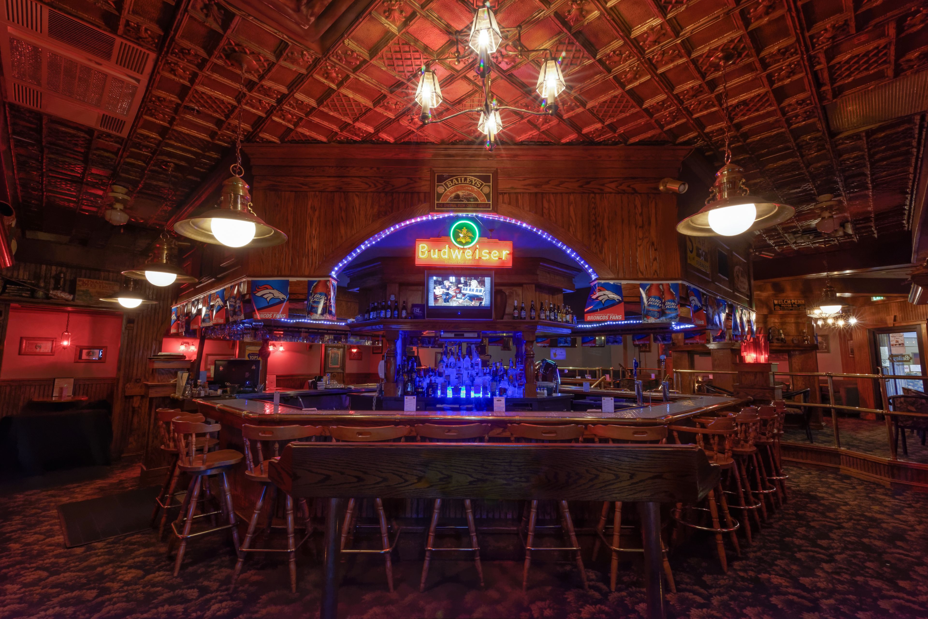 Zona de bar con techo de madera, taburetes y un letrero de neón de Budweiser.