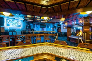 Uma área de bar com mobiliário de madeira, um letreiro de neon para Bailey's Live e um palco para apresentações ao vivo.