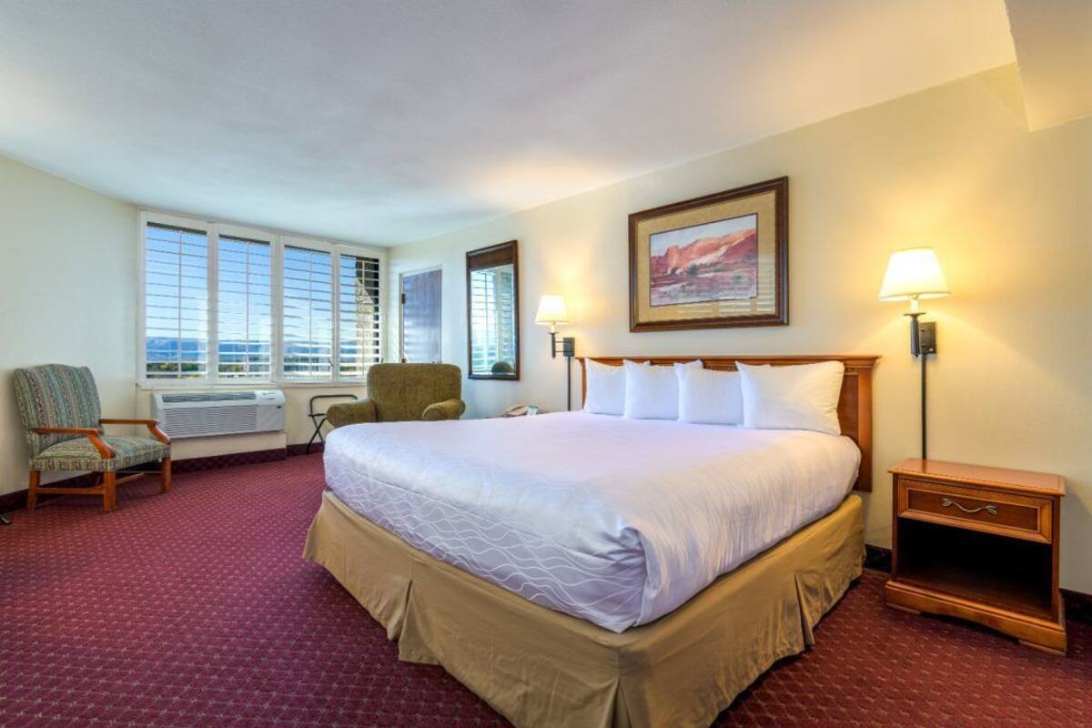 A hotel room with a large bed, two chairs, a desk, and a window with a view.