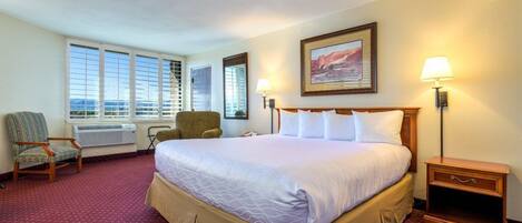 A hotel room with a large bed, two chairs, a desk, and a window with a view.