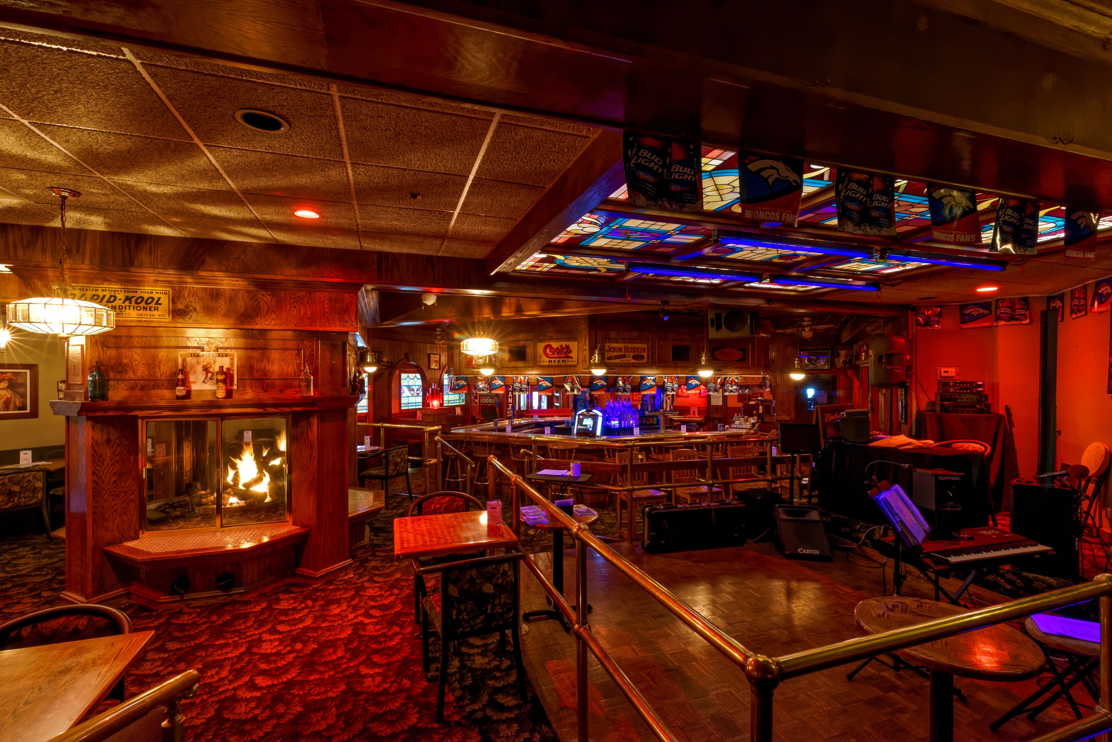 Zona de bar con chimenea, taburetes y escenario con equipo musical.