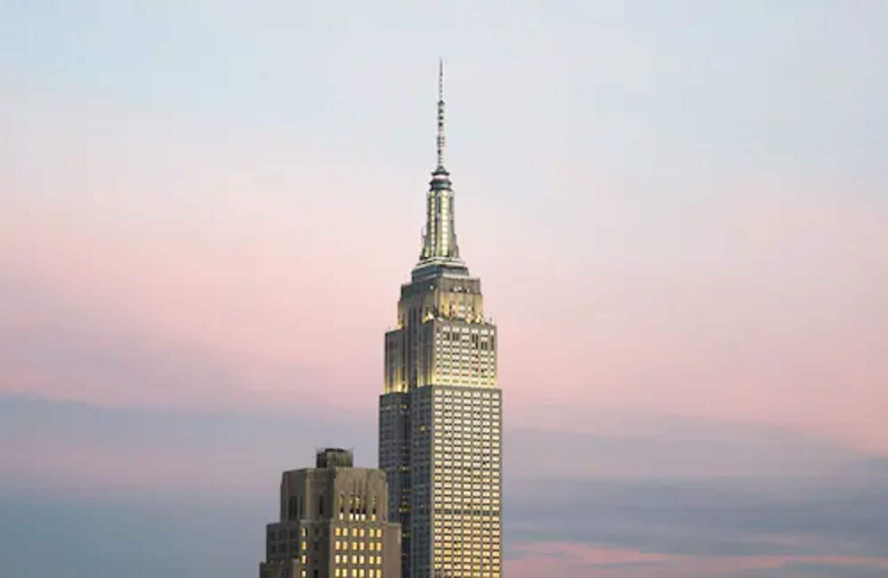 A high-rise building with a prominent spire, likely a hotel or office building, against a sky with soft pink and blue hues.