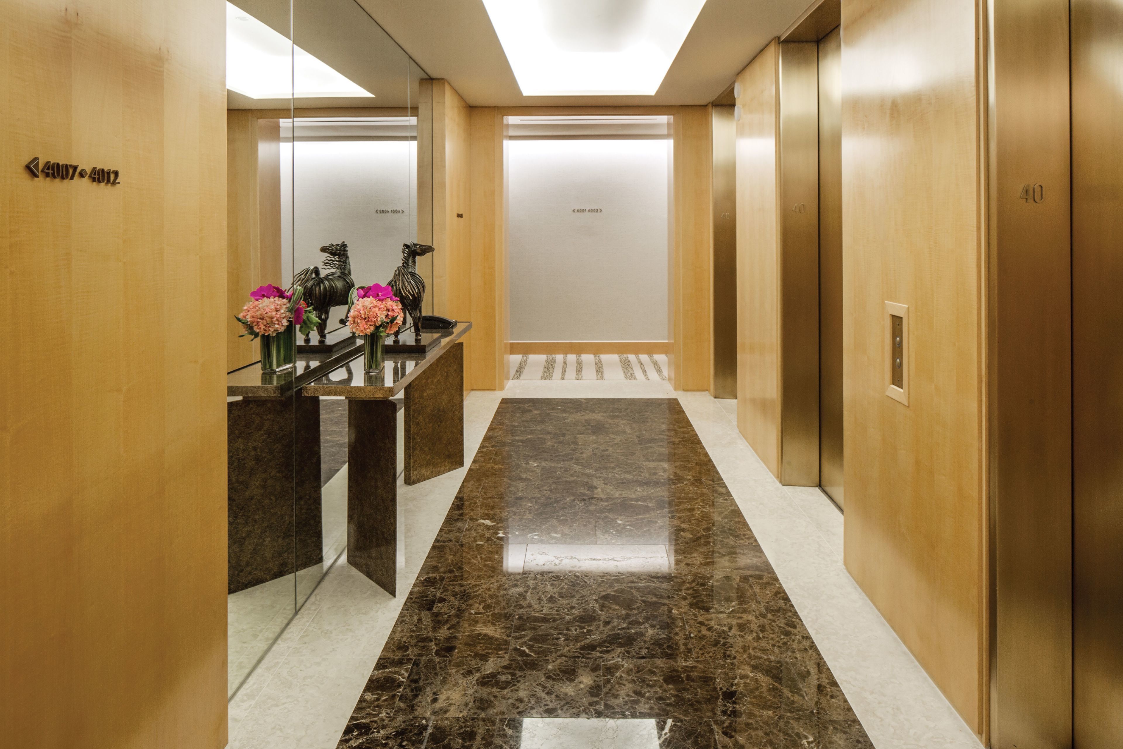 A modern hotel lobby with a marble floor, wooden walls, and a reception desk with floral arrangements.