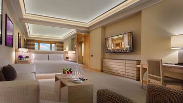 A hotel room with a large bed, a desk, a chair, a sofa, and a TV.