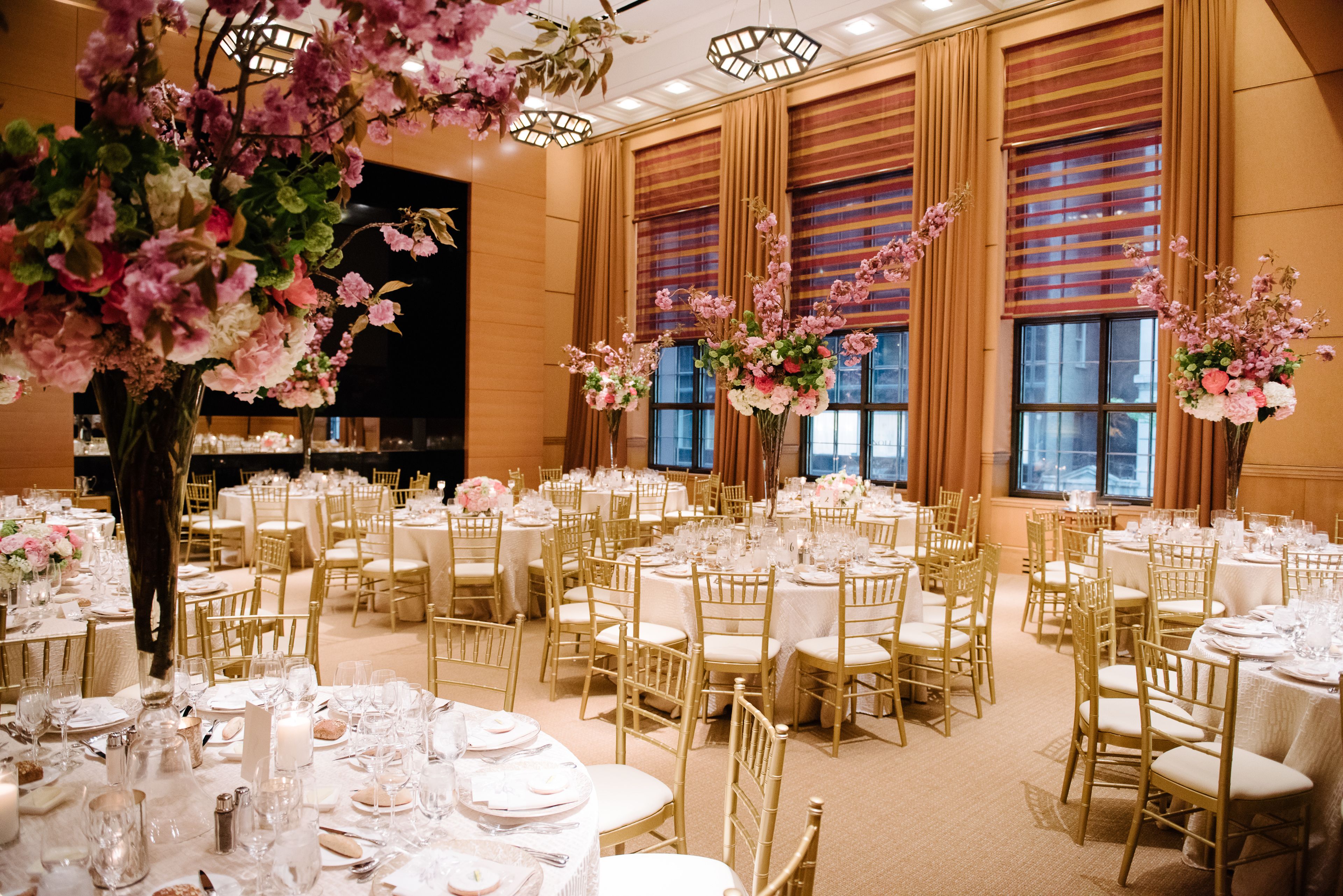 Een feestzaal met ronde eettafels, gouden stoelen en bloemrijke decoraties.