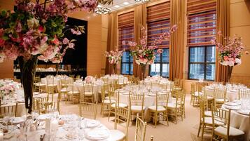 A banquet hall with round tables set for dining, gold chairs, and floral centerpieces.