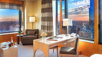 A hotel room with a city view, a dining table, a sofa, and a desk with a lamp.