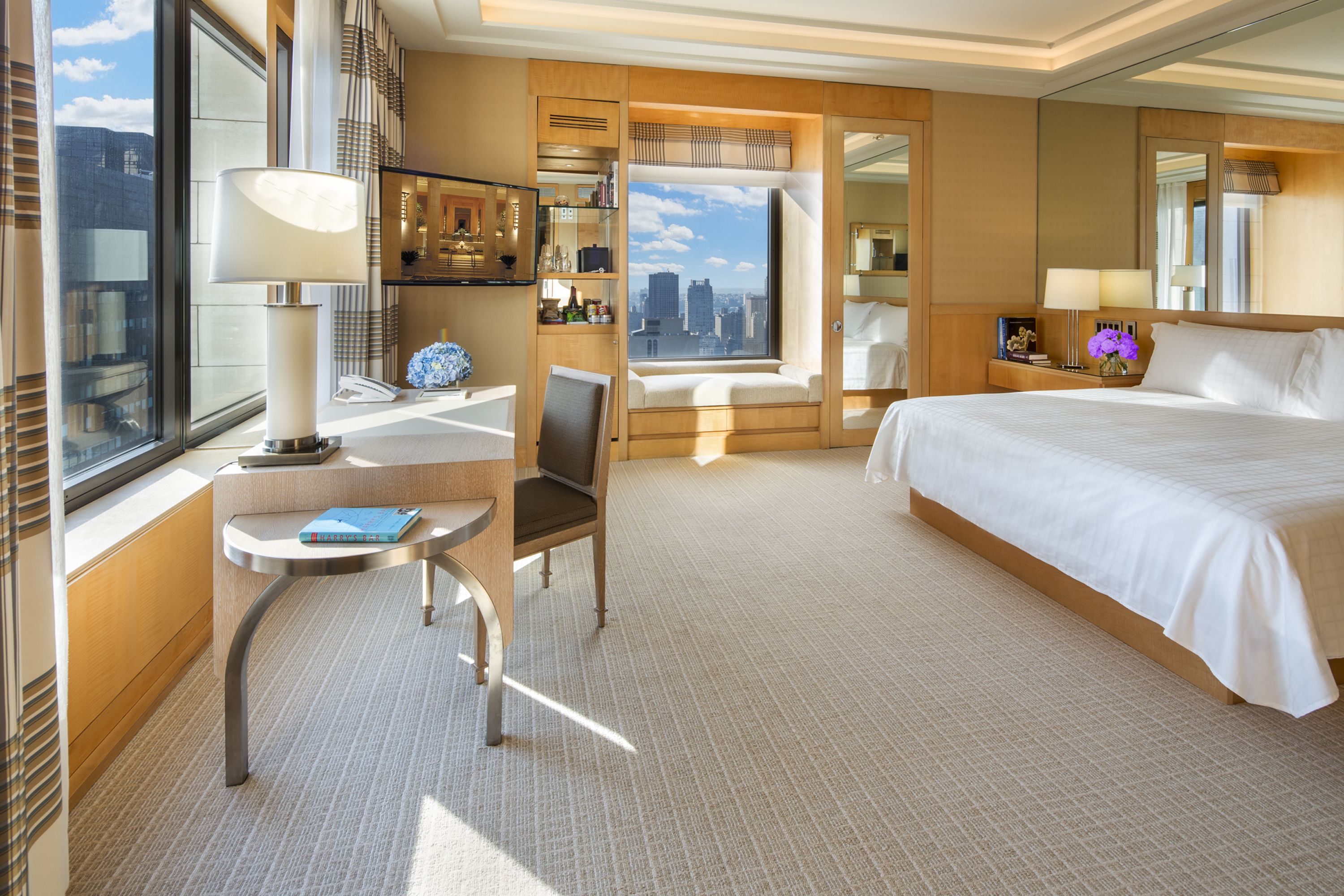 Habitación de hotel con una cama grande, un escritorio con silla, una ventana con vista a la ciudad y un baño con espejo.