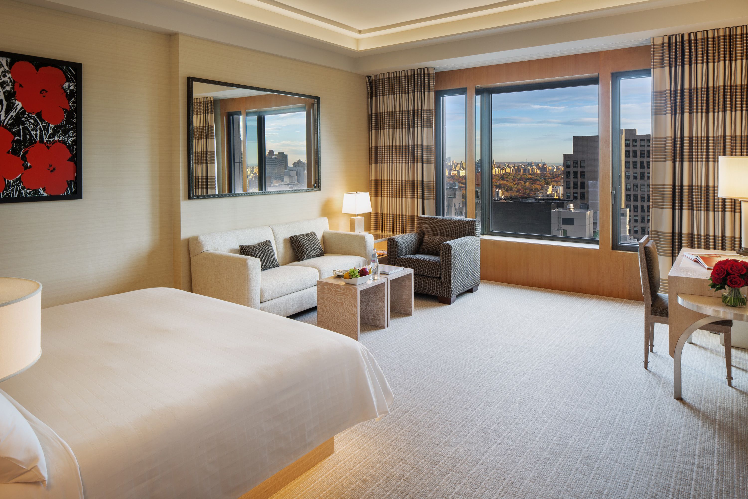 Une chambre d’hôtel avec un lit, un canapé, une chaise, une petite table et une vue sur la ville.