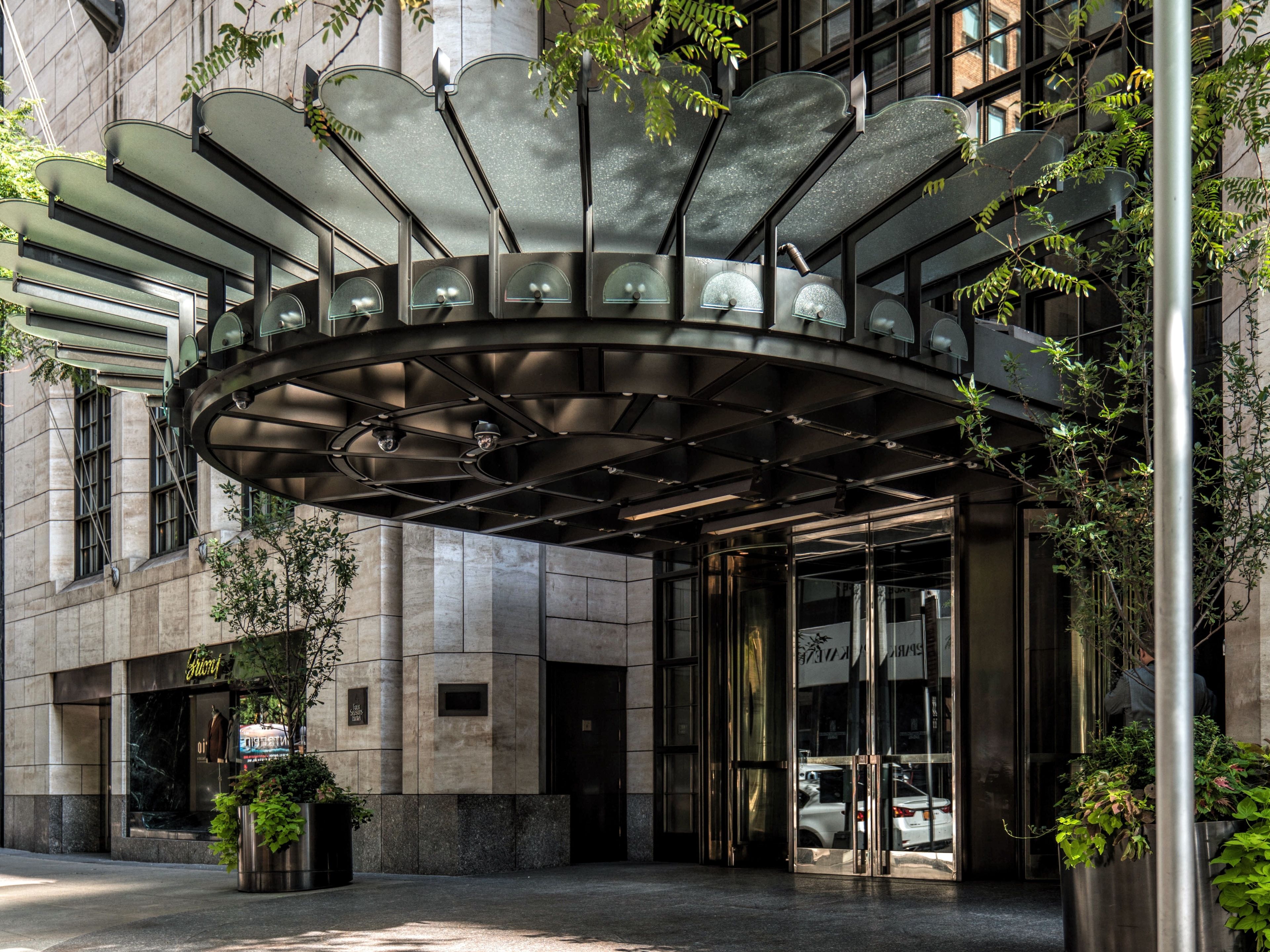 A modern building entrance with a curved glass canopy, large windows, and a stone facade.