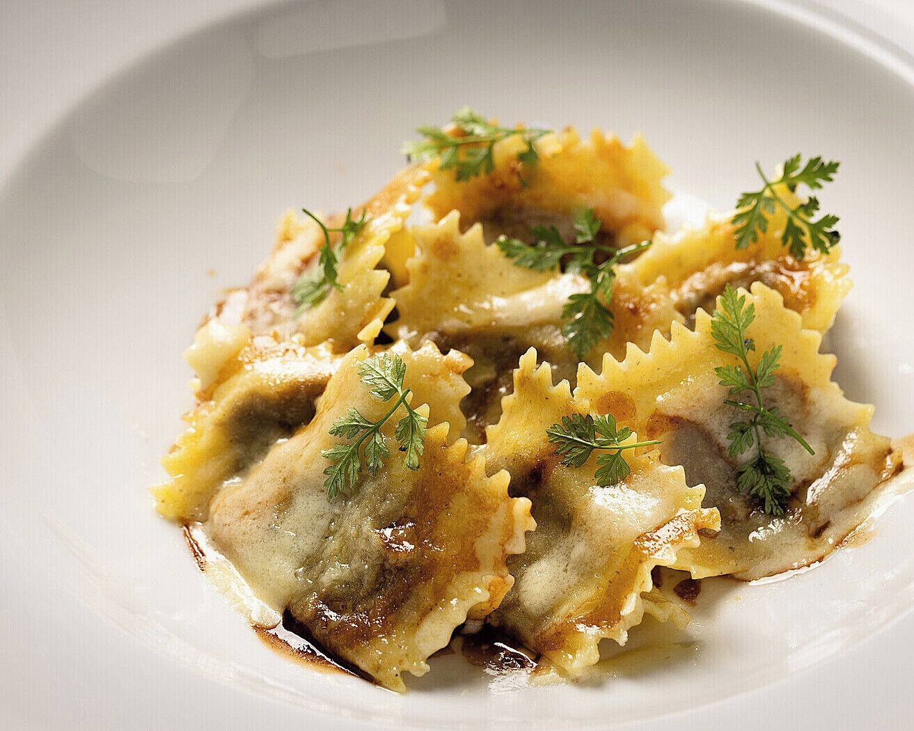 A plate of ravioli with a creamy sauce and garnished with parsley.