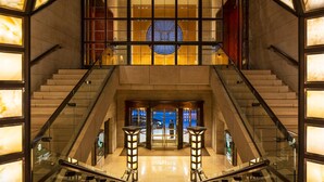 Eine moderne Hotellobby mit einer zentralen Treppe, Glasgeländern und einem großen, runden Oberlicht.
