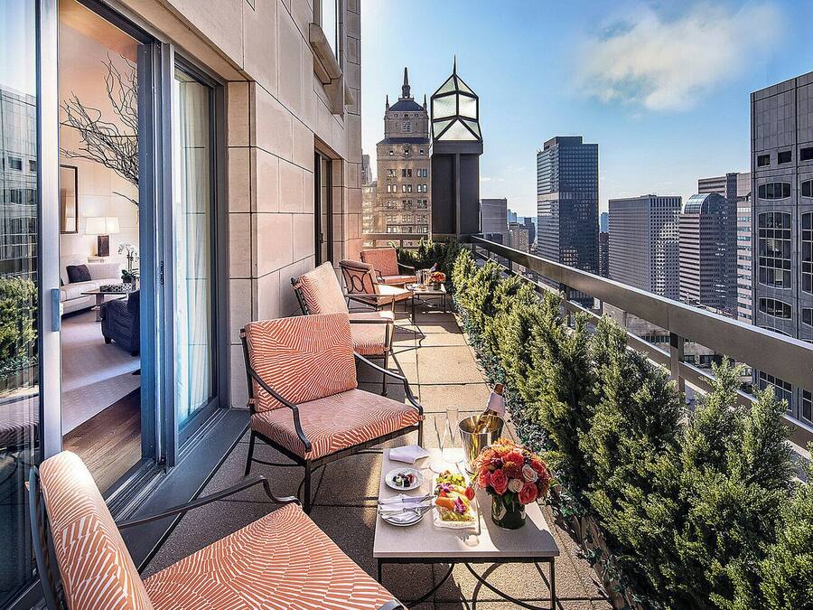 Varanda com área de estar externa, uma mesa com arranjo floral e vista para a cidade.
