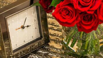 Un reloj y un jarrón con rosas rojas sobre una superficie reflectante.