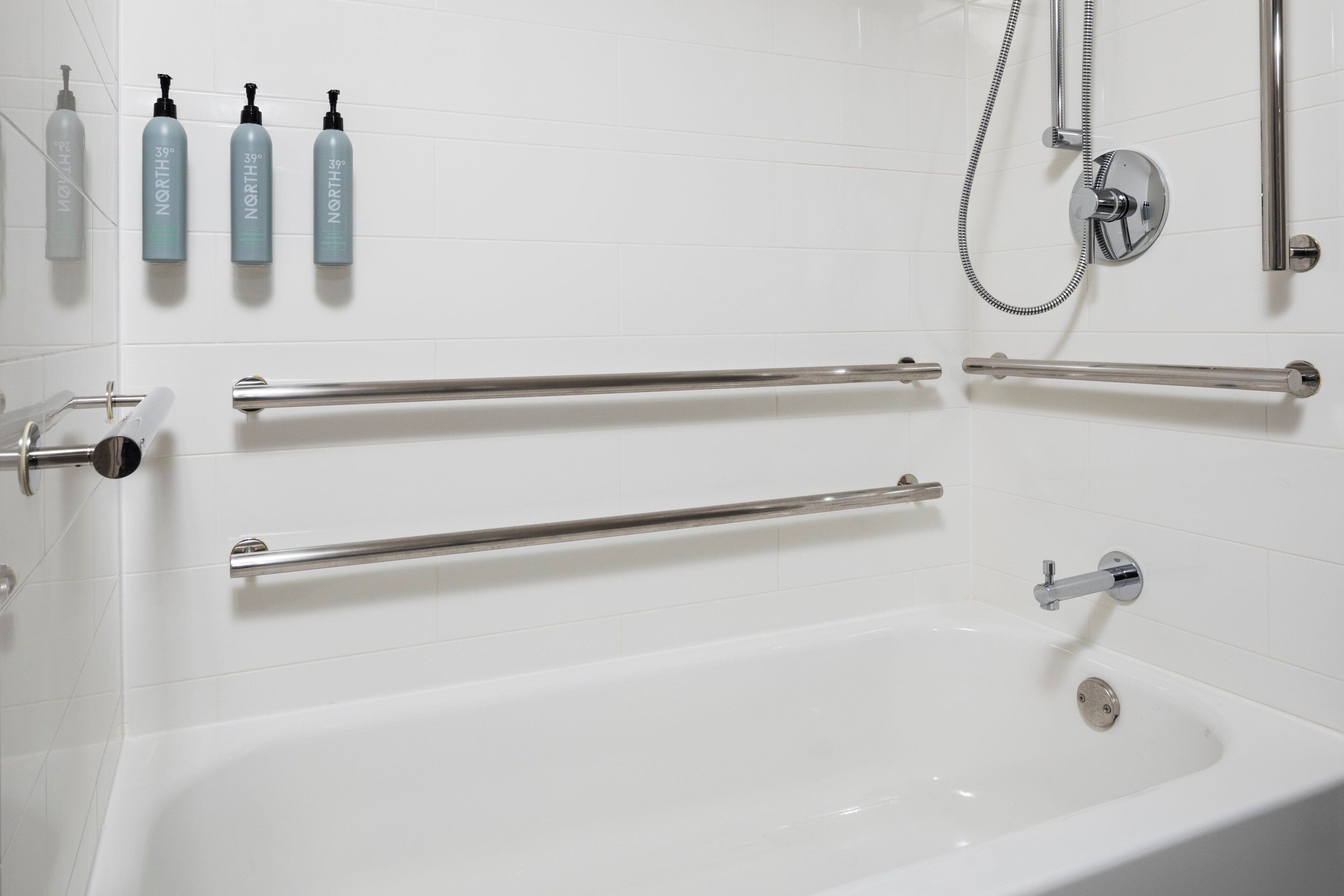 A modern bathroom with a bathtub, grab bars, and a showerhead.