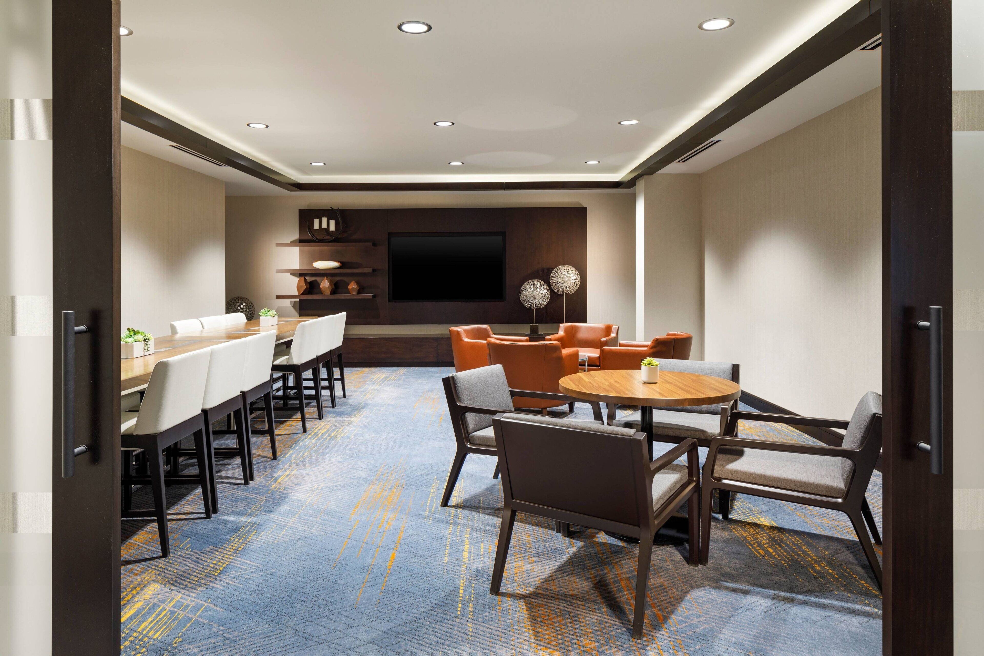 A modern hotel room with a large bed, a desk, and a seating area with chairs and a table.