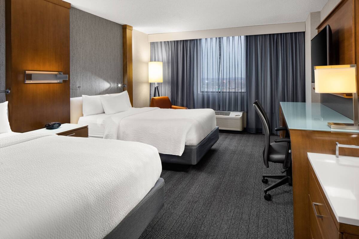 Een hotelkamer met twee bedden, een bureau, een stoel, een televisie en een raam met gordijnen.